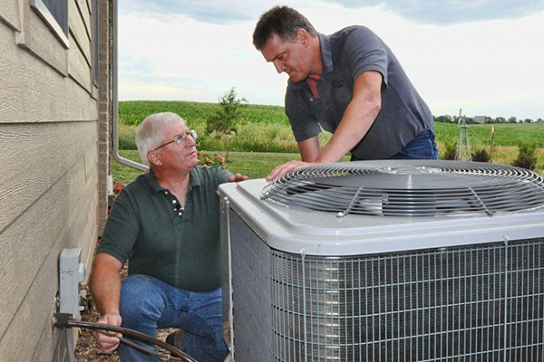 Two HVAC techs work together on exterior compressor unit
