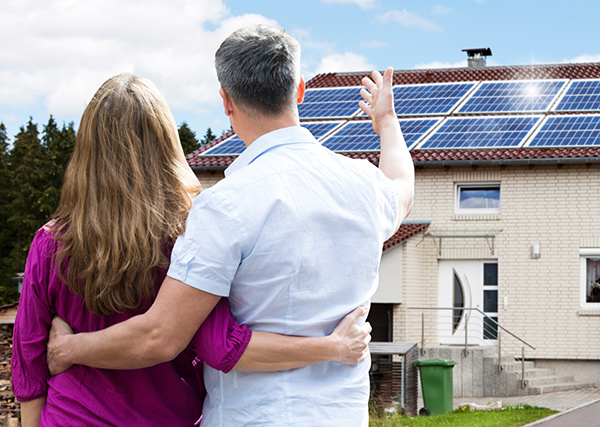 Couple looking at their new roof-mounted solar panels on top of white brick house