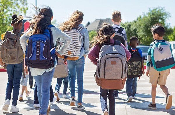 Several school-aged children walking away from camera wearing backpacks.