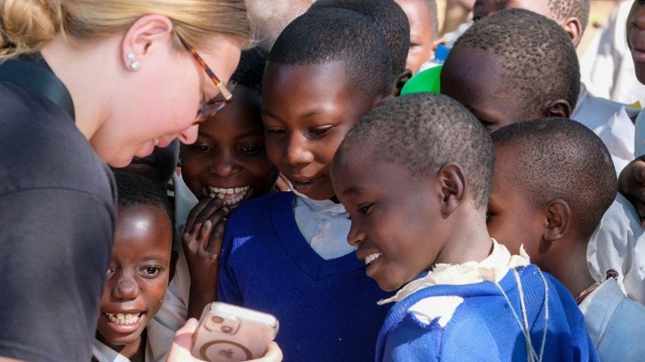 Children gather around a woman holding a cell phone