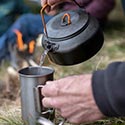 Teekrug schenkt heisses Wasser in einen Outdoorbecher