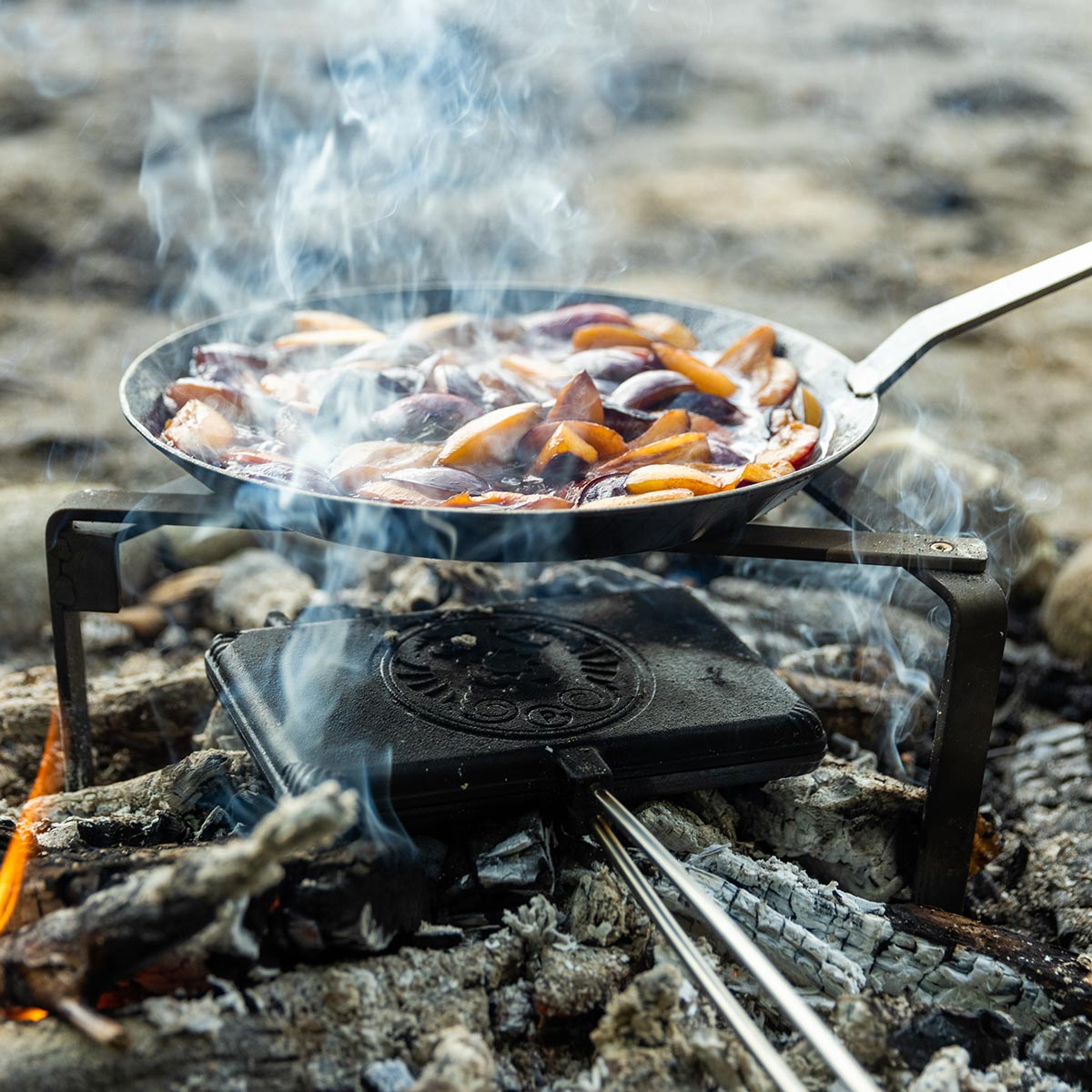 Eine Pfanne mit Zwetschgenkompott und ein Waffeleisen mit Waffeln über dem Feuer