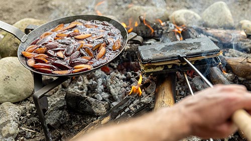 Eine Pfanne mit Zwetschgenkompott und ein Waffeleisen mit Waffeln über dem Feuer