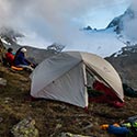 MSR-Zelt steht auf dem Gipfel, im Hintergrund sitzen drei Menschen vor einer Bergkulisse