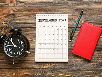 A desk with the September calendar, an alarm clock, a pen, and a notebook