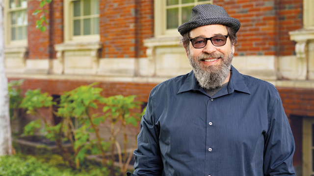 Tarik Elseewi, wearing a dark blue shirt, gray hat and dark glasses, standing in front of a brick building.