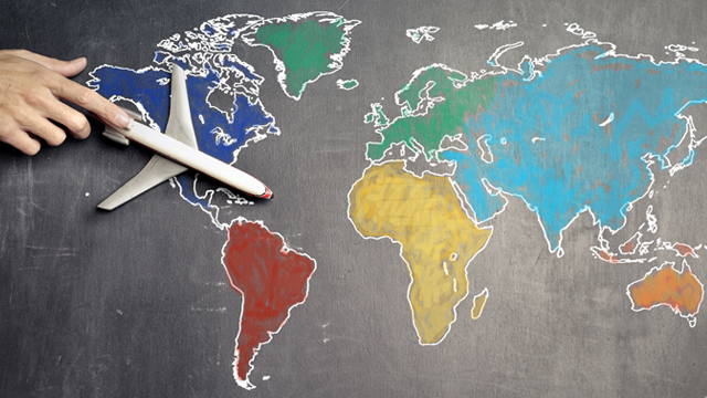 A hand entering the frame points to a model airplane sitting on top of a chalk-drawn map of the continents of the world.