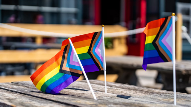 Three small rainbow flags displayed on top of a picnic table.