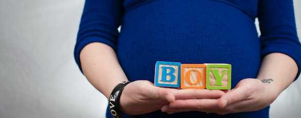 A pregnant woman holding blocks spelling 'boy'