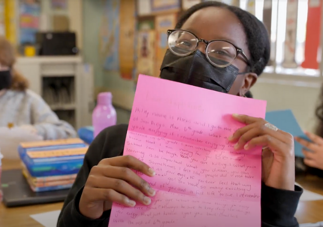 Image of a young student from Perkins Elementary School holding up a letter written by a USD student