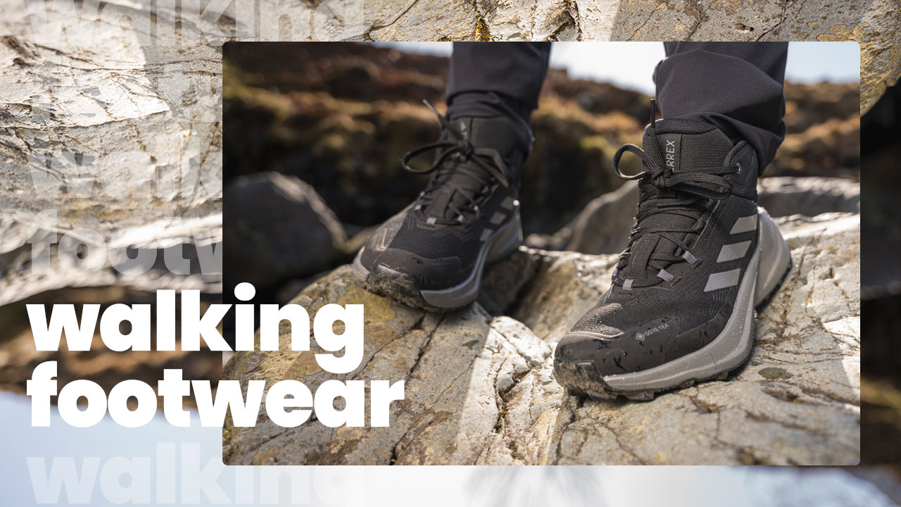 A closeup photo of a pair of black and grey walking boots. The subject is stood on a rock.