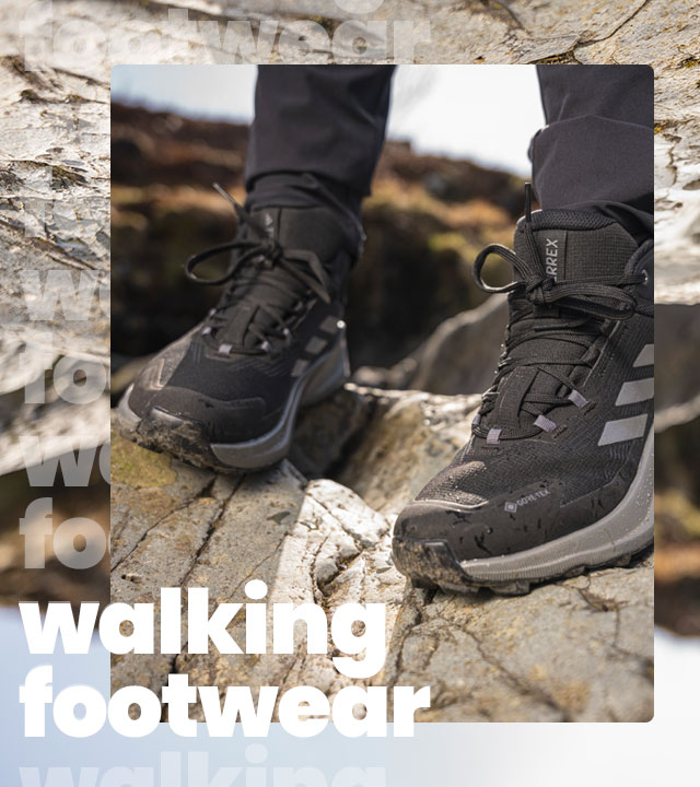 A closeup photo of a pair of black and grey walking boots. The subject is stood on a rock.