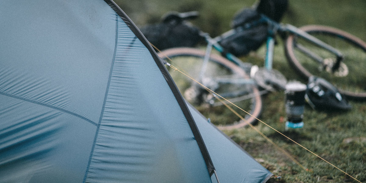 A blue tent pitched up with a bike resting on the floor next to it.