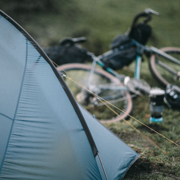 A blue tent pitched up with a bike resting on the floor next to it.