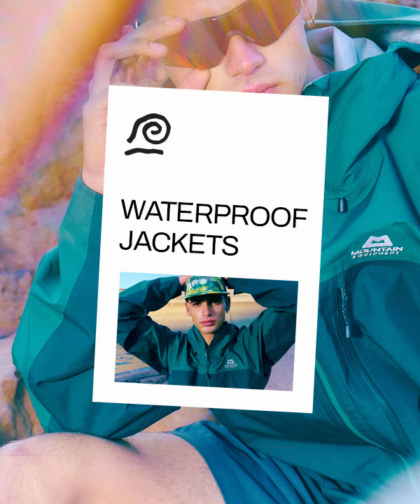 A person wearing a two-tone green waterproof jacket holding their hand on their head.