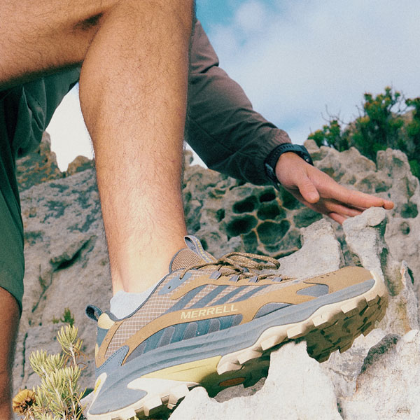 Close-up of a Merrell hiking shoe stepping onto rocky terrain, showing rugged sole and outdoor setting.