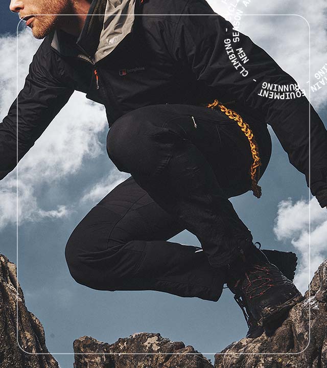 Man hiking leaning on Rocks wearing trousers and a waterproof jacket