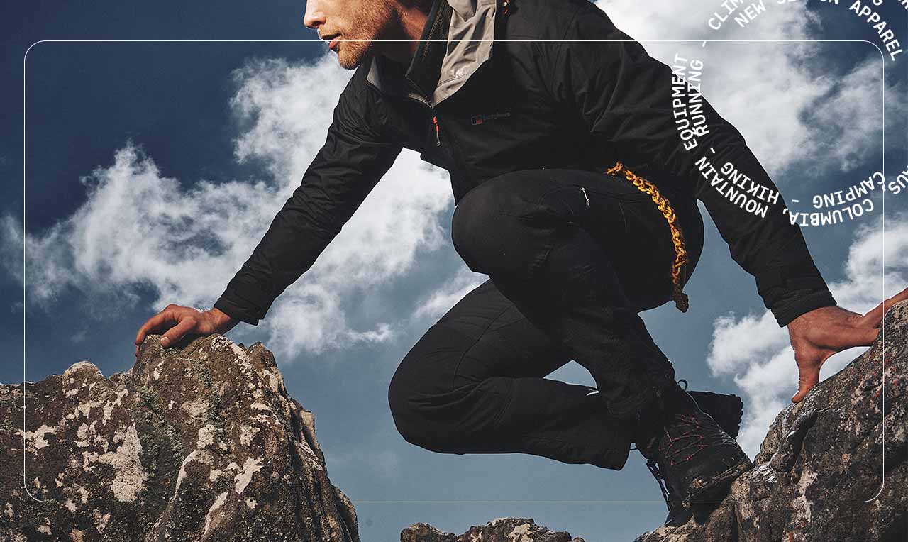 Man hiking leaning on Rocks wearing trousers and a waterproof jacket
