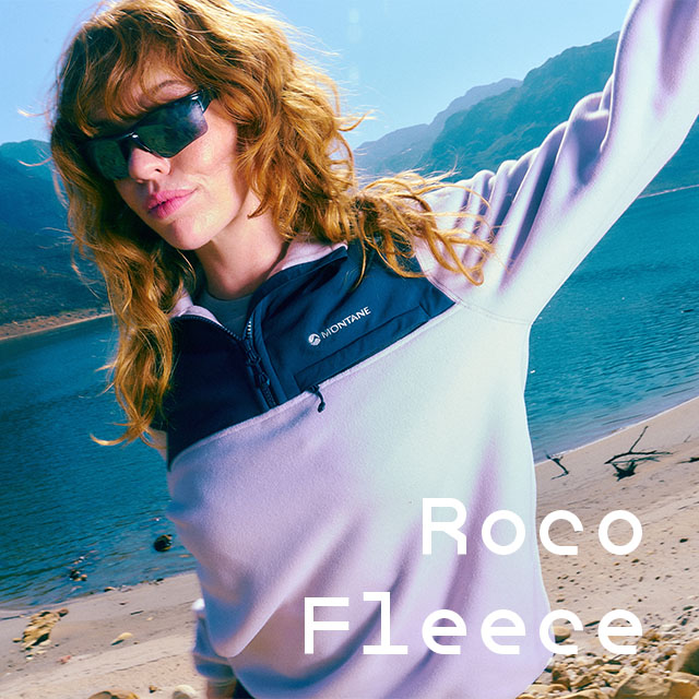 Woman wearing Montane Roco fleece, wearing sunglasses with a lake Iin the background
