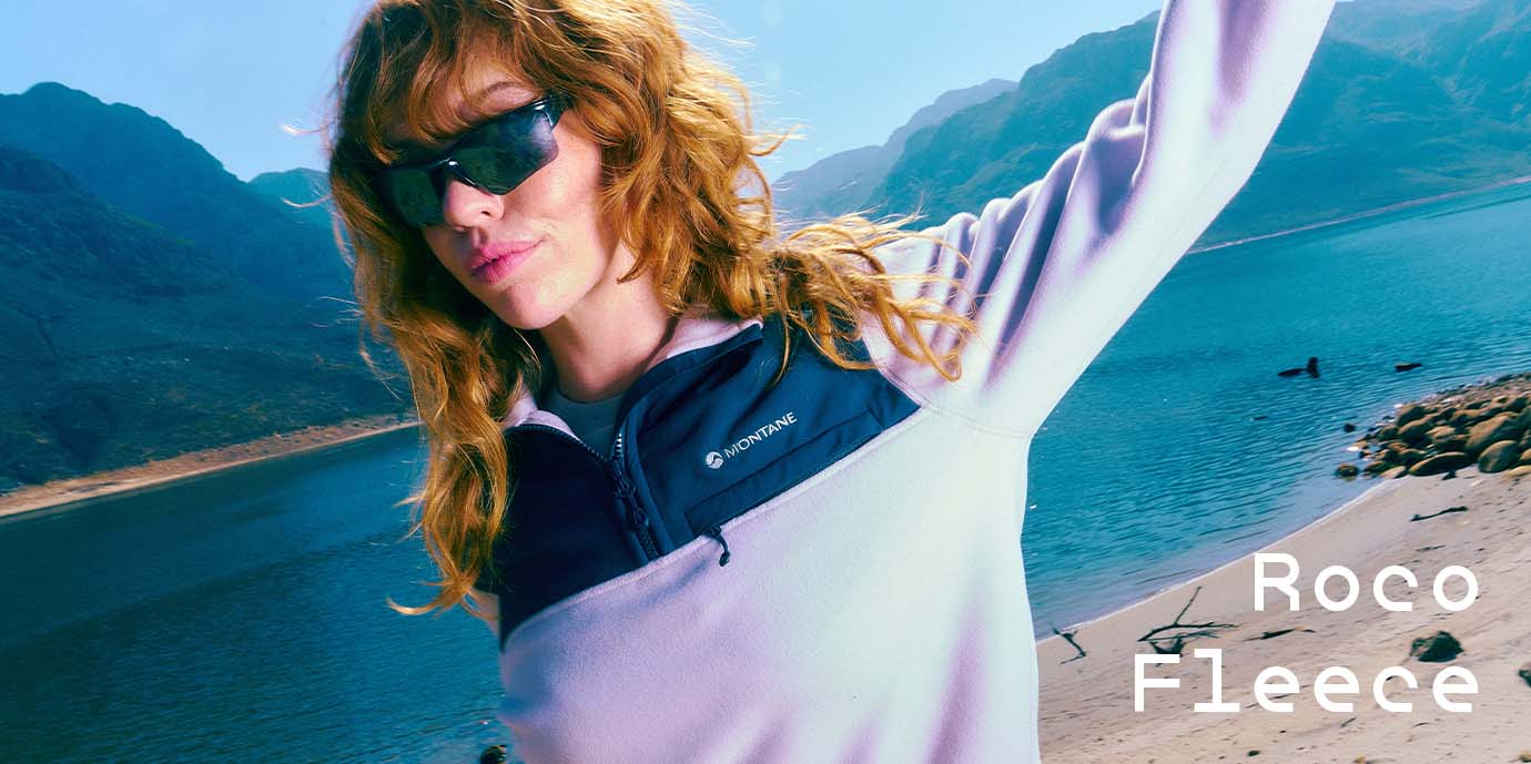 Woman wearing Montane Roco fleece, wearing sunglasses with a lake Iin the background