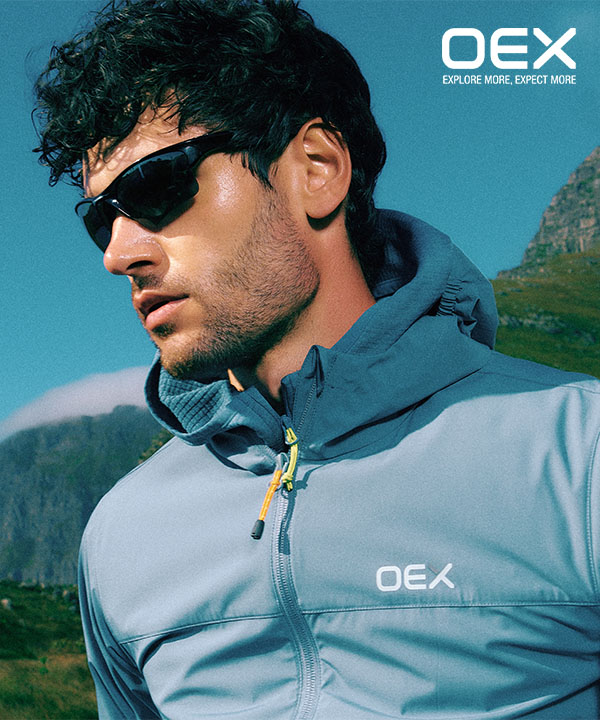 Man wearing OEX jacket and sunglasses with mountains in the background