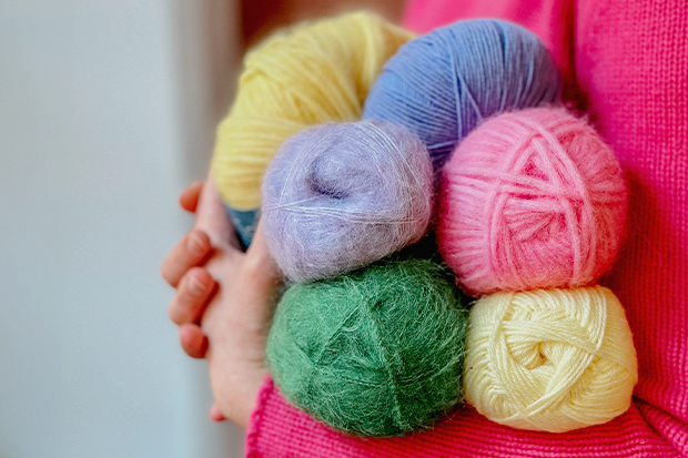 Bilde av en hånd som holder flere garnnøster i rosa, blått, grønt, gult og lilla.