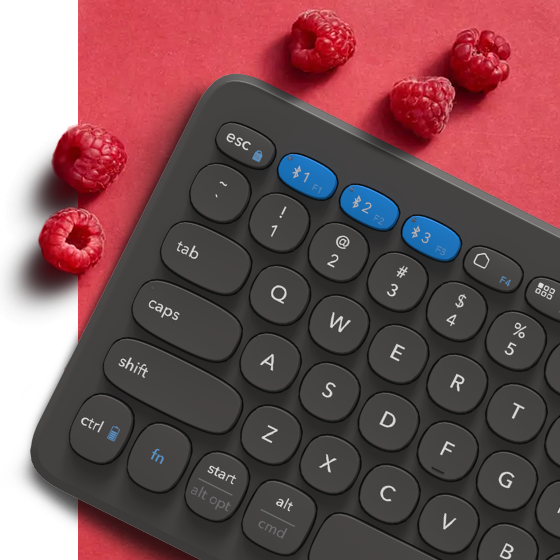 Keyboard on a light red backround surrounded by raspberries