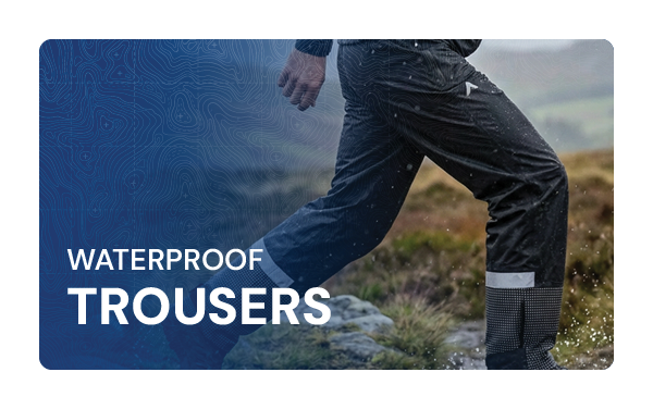 WATERPROOF TROUSERS: A man walks through a rainy glen wearing Altura Men's Night Vision Waterproof Overtrousers in Black. 