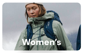 WOMEN'S. A woman hikes wearing a Rab Women's Firewall Mountain Jacket in Green. 