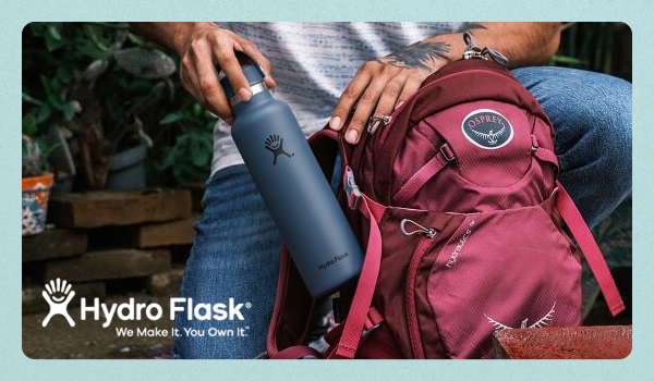 HYDRO FLASK: We Make It, You Own It. A man tucks a Hydro Flask 21oz Standard Mouth Water Bottle into the side pocket of an Osprey pack.