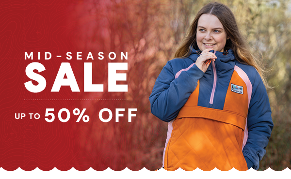 MID-SEASON SALE: UP TO 50% OFF. A woman walks in the woods, zipping up a Passenger Women's Ocean Insulated 1/2 Zip Jacket in Navy/Orange