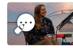 Tiso blog. A woman wearing a blue patterned fleece and green trousers sits outside a tent with a camp mug. A white graphic of a pencil writing a note features on the left of the image.