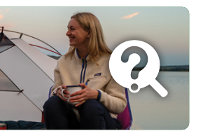 Shopping guides. A woman wearing a cream fleece and black trousers sits outside a tent with a camp mug. A white graphic of a ? on a magnifying glass features on the right of the image.