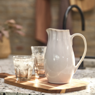Fehér kerámia kancsó és üveg poharak fa vágódeszkán