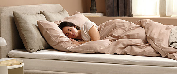 Egy nő alszik egy bézs ágyneművel beágyazott ágyon