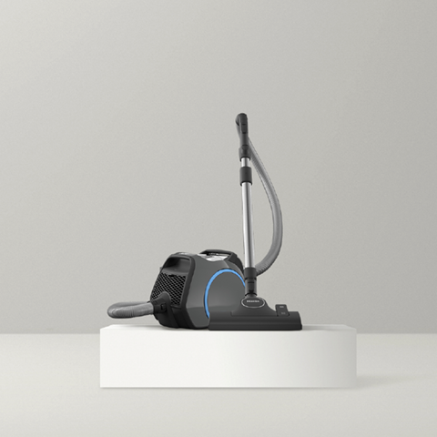 Miele bagged canister vacuum on white pedestal against gray background
