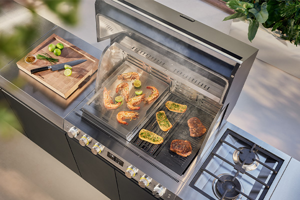 Die Miele Outdoor-Küche mit vielseitigem Zubehör, auf dem Steaks, Meeresfrüchte und Kräuterbaguette zubereitet werden.