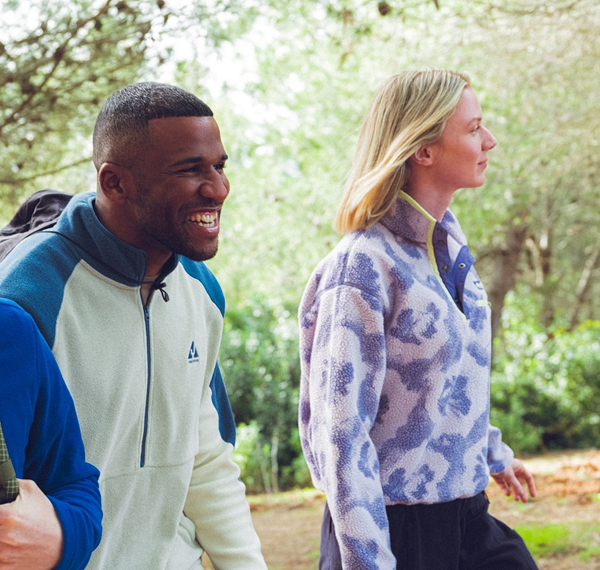 Afbeelding van een vrouw en een man wandelend door het bos met fleecevesten aan