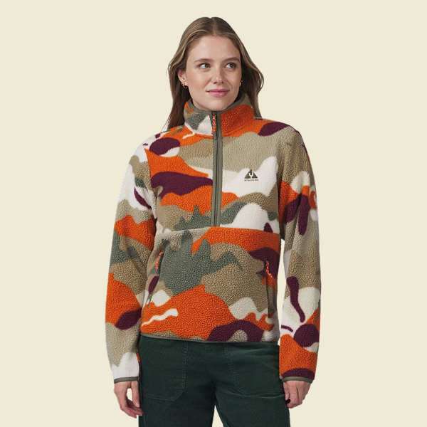 Persoon draagt een kleurrijke fleece trui met opvallend oranje, bordeauxrode en groene print.