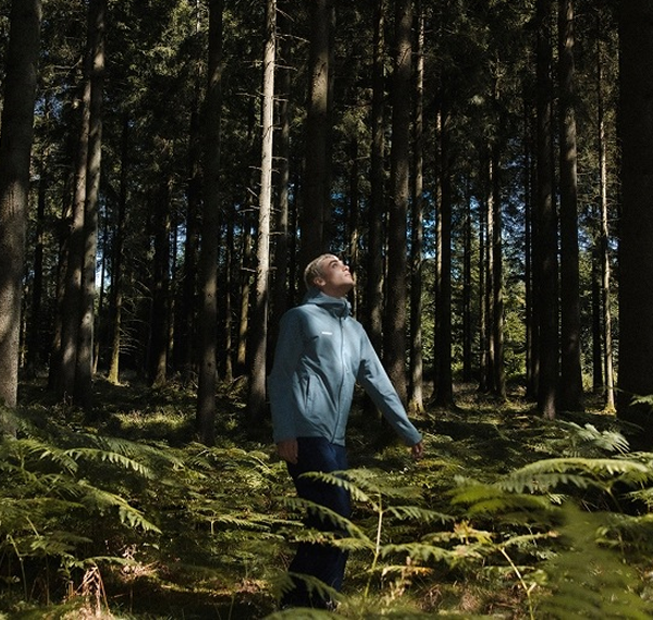Man in het bos met een blauwe jas aan.