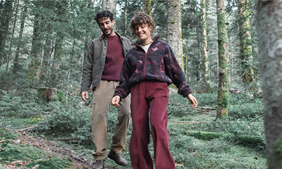 Twee personen wandelen door een bos in comfortabele outdoor kleding uit de nieuwe collectie.