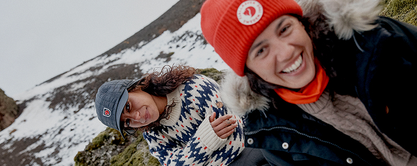 Twee personen in warme outdoor kleding in een bergachtig landschap met sneeuw op de achtergrond.