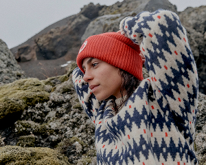 Persoon draagt een gebreide sweater met patroon en een oranje muts in een rotsachtig berglandschap.