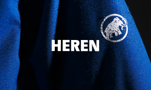 Detail van een blauwe waterdichte jas met regendruppels en de tekst ‘HEREN’.