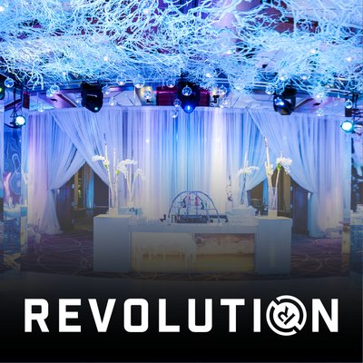 An immersive event installation features blue lighting, draped fabric and a central display table.