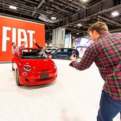 A person takes a photo of two people posing inside a red Fiat car at the Washington Auto Show.