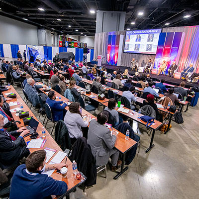 A conference hall with people attentively watching a panel presentation.