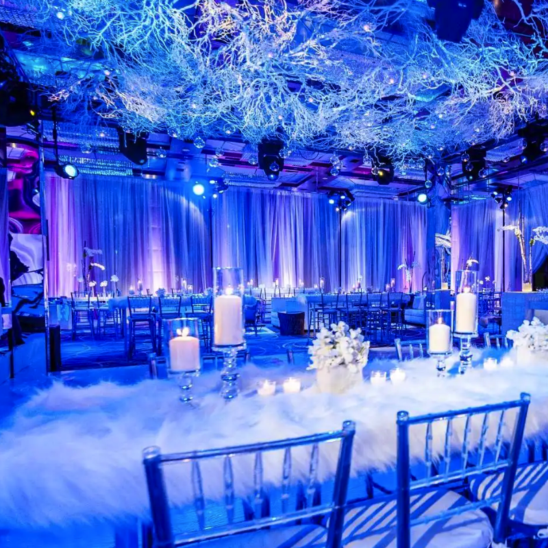 Elegant event space with blue lighting, candlelit tables and decorative branches hanging from the ceiling.