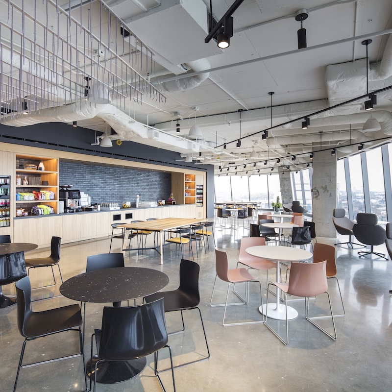 Modern office cafe with sleek seating, snack shelves and panoramic windows.