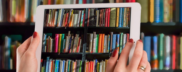 Tablette électronique tenue par une femme devant des étagères de livres
